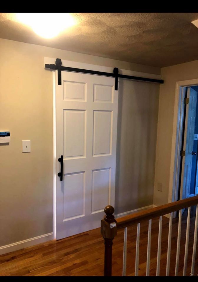 White barn door with black hardware in a hallway setting.
