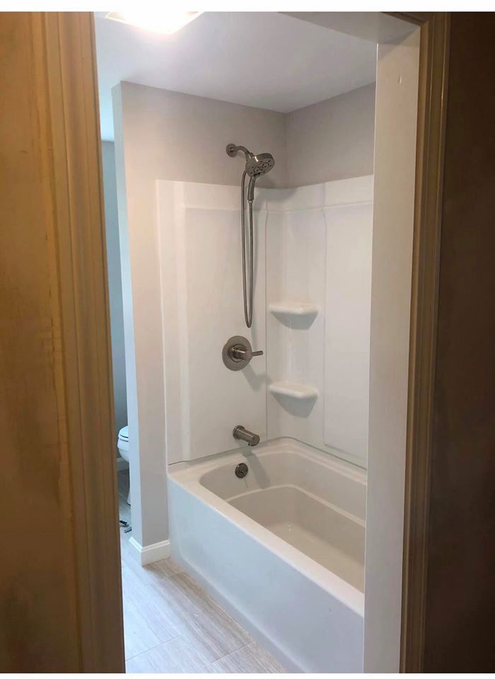 White bathtub/shower combo in bathroom. Gray walls, brown door frames, silver showerhead.