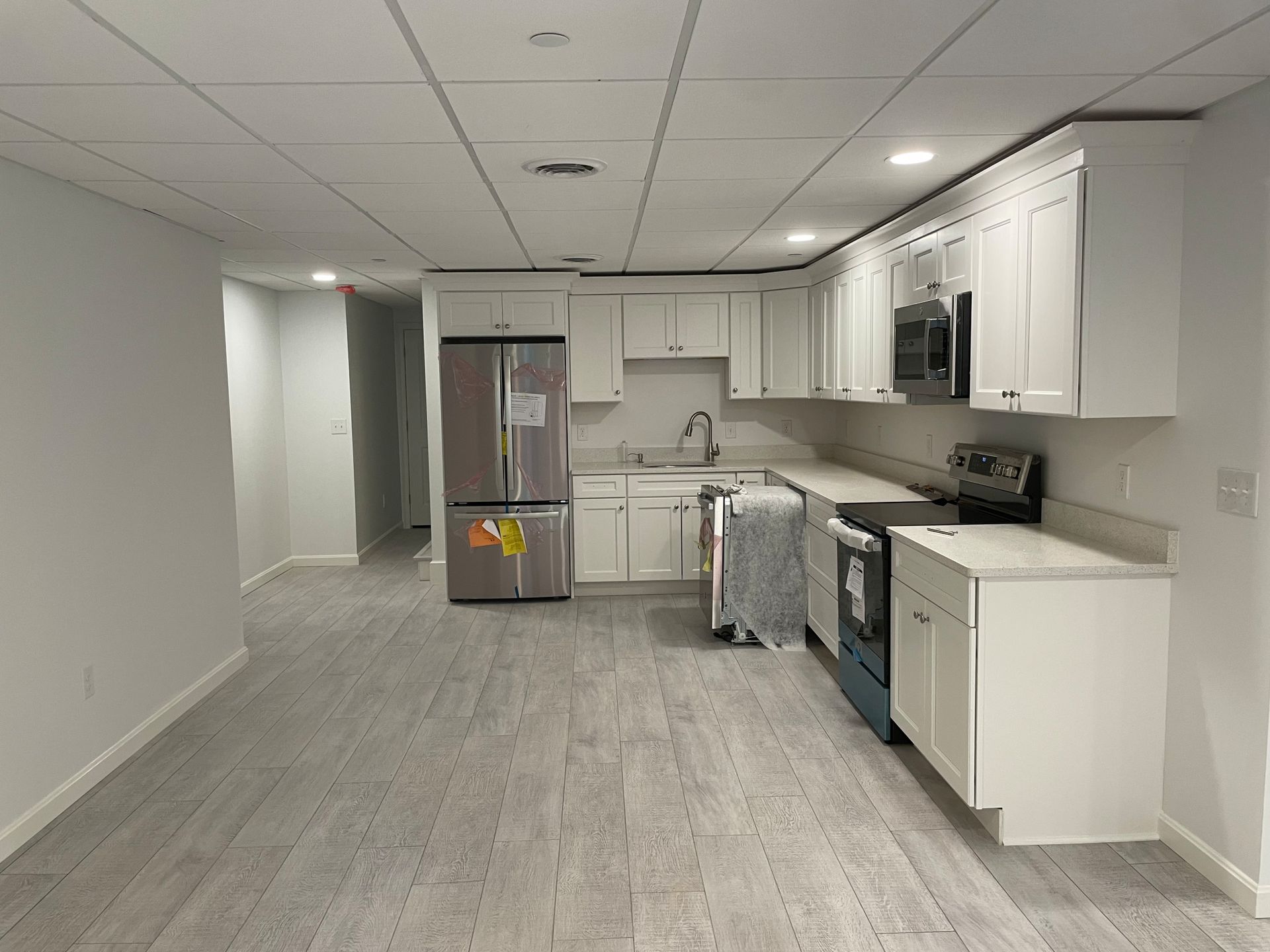 A kitchen with white cabinets and appliances, light gray flooring, and a stainless steel refrigerator.