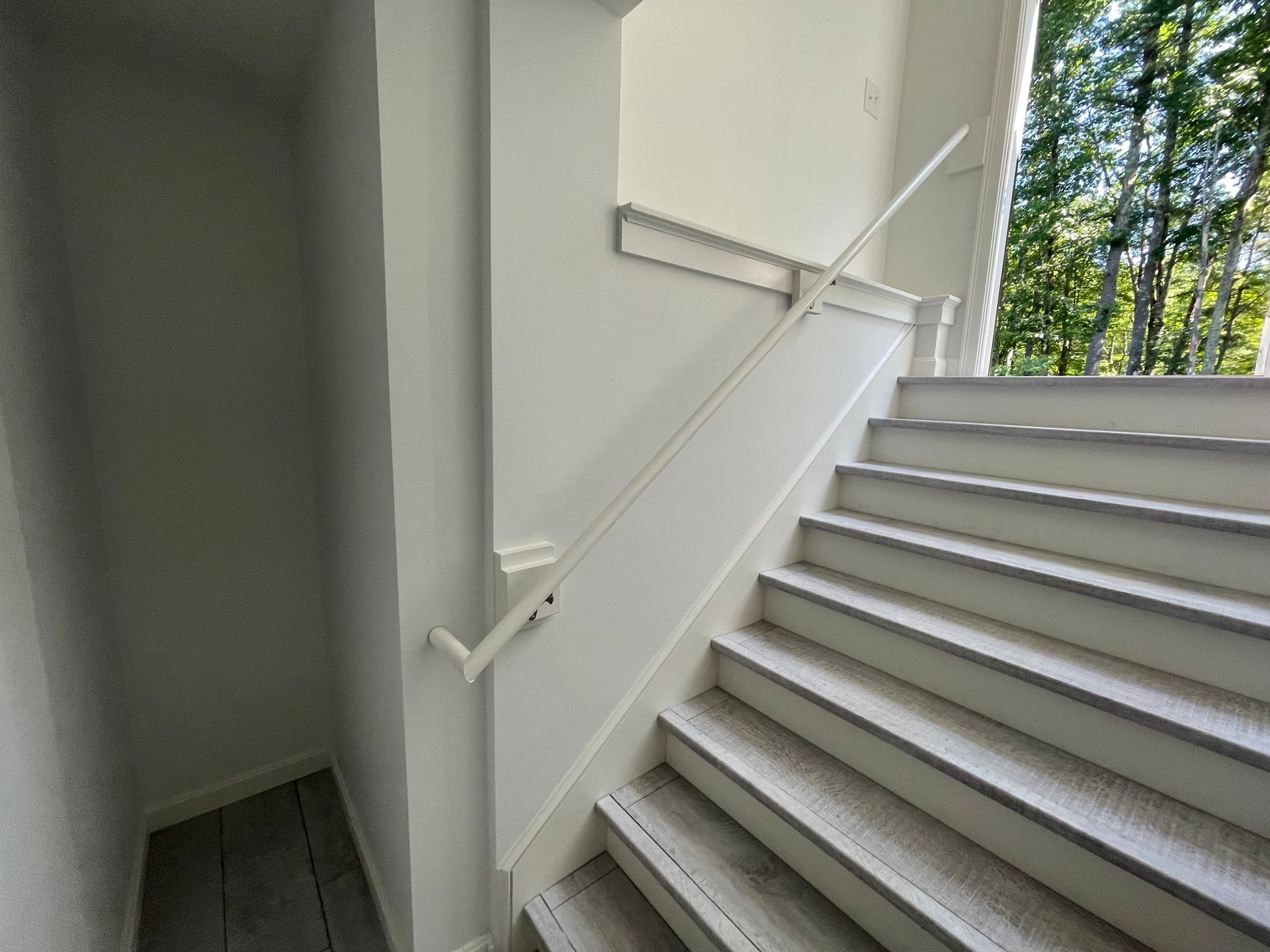 White staircase with handrail against a white wall, leading upward; adjacent to a wall and outdoors.