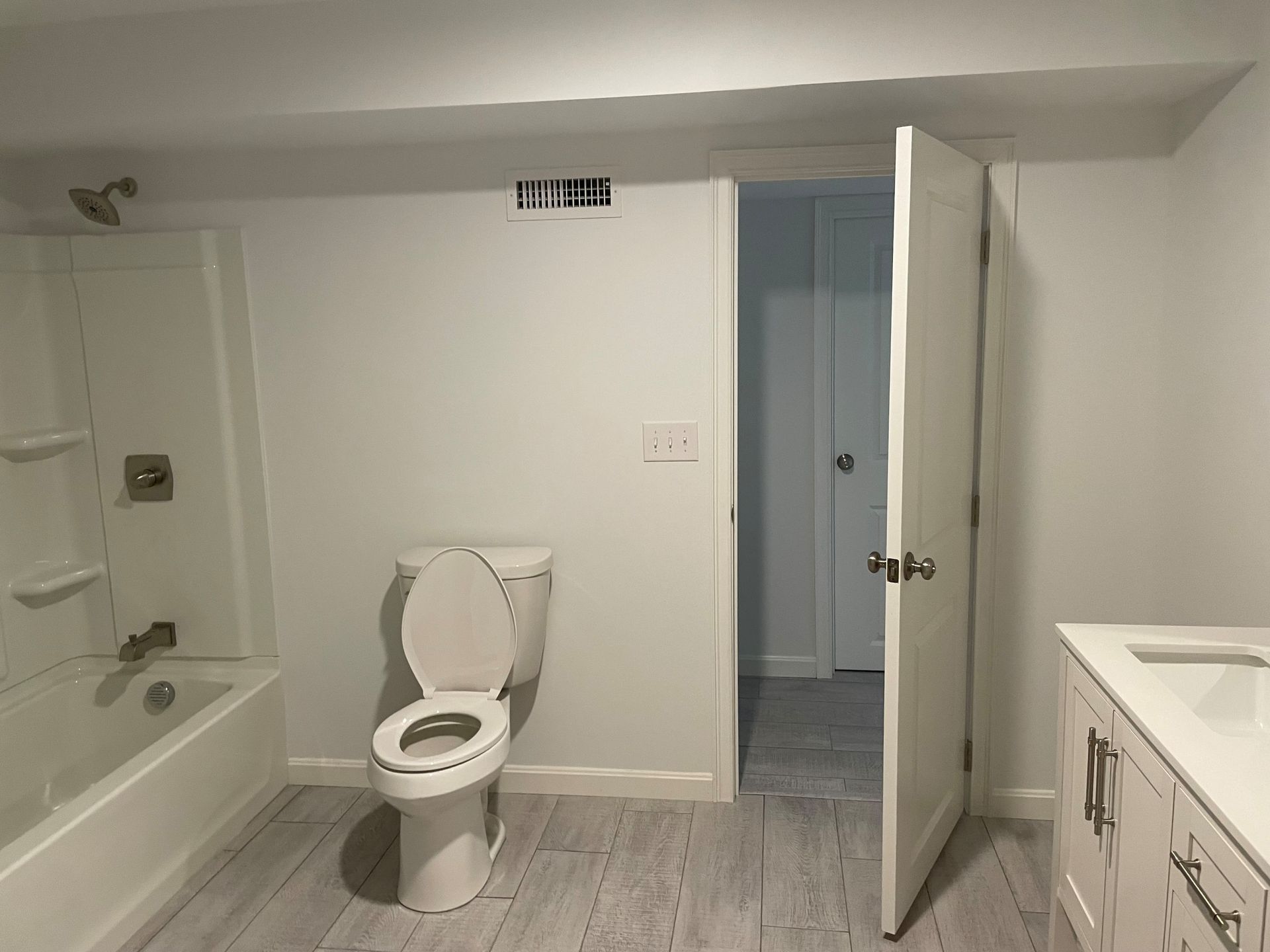White bathroom with toilet, tub, open door to hall, and vanity.