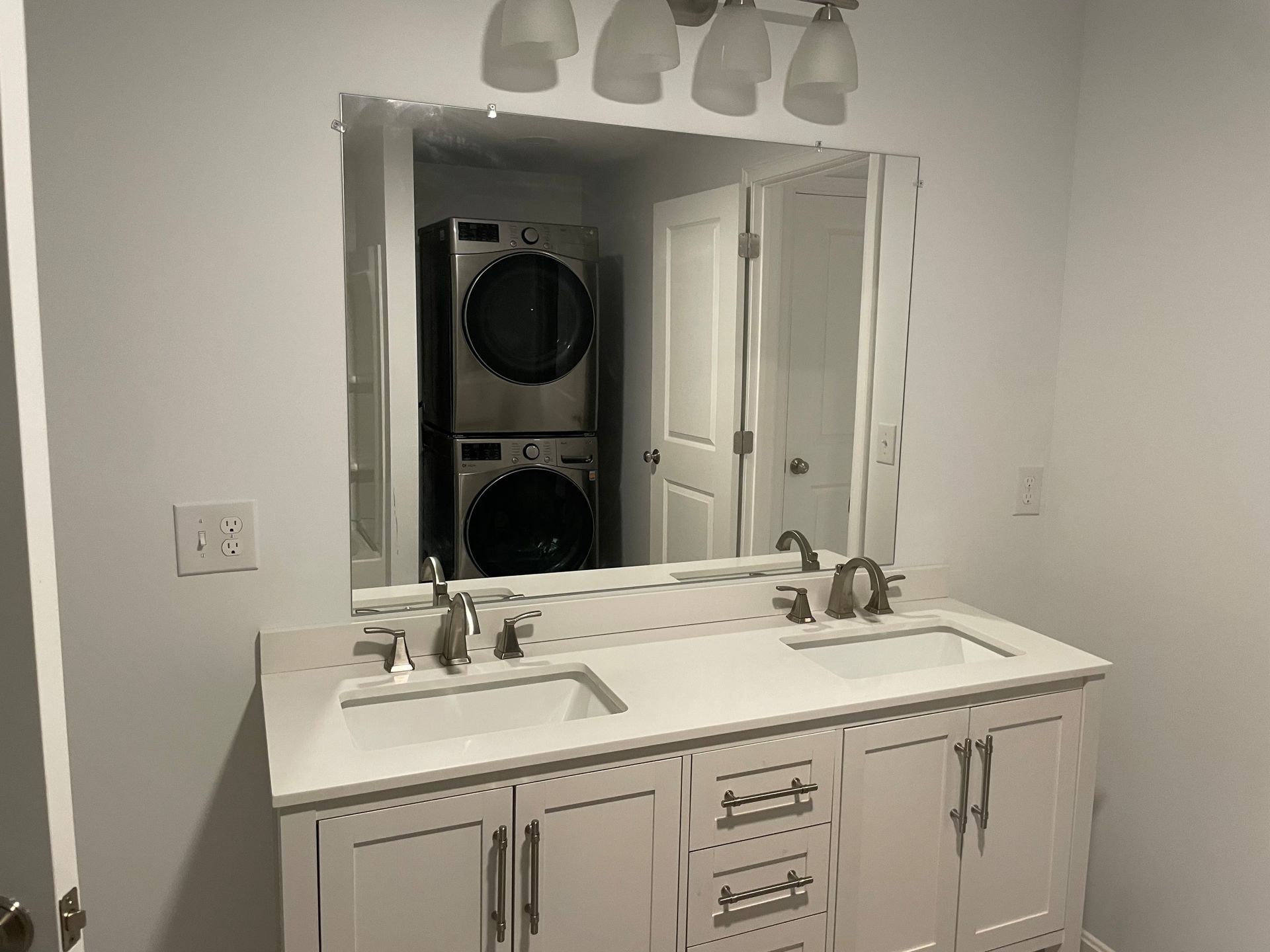 Bathroom with double vanity, mirror reflecting laundry machines and doorway.