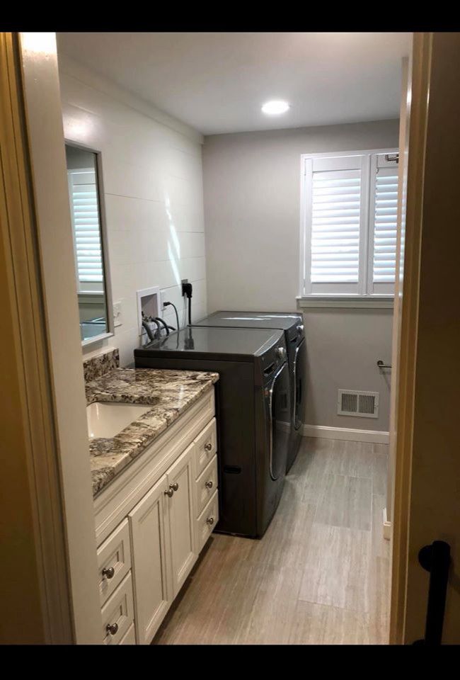 Laundry room with white cabinets, granite countertop, and dark gray washer/dryer.  Shutters on window.