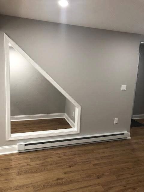 A room with a mirrored triangular cutout, white trim, and wooden floors. Gray walls.