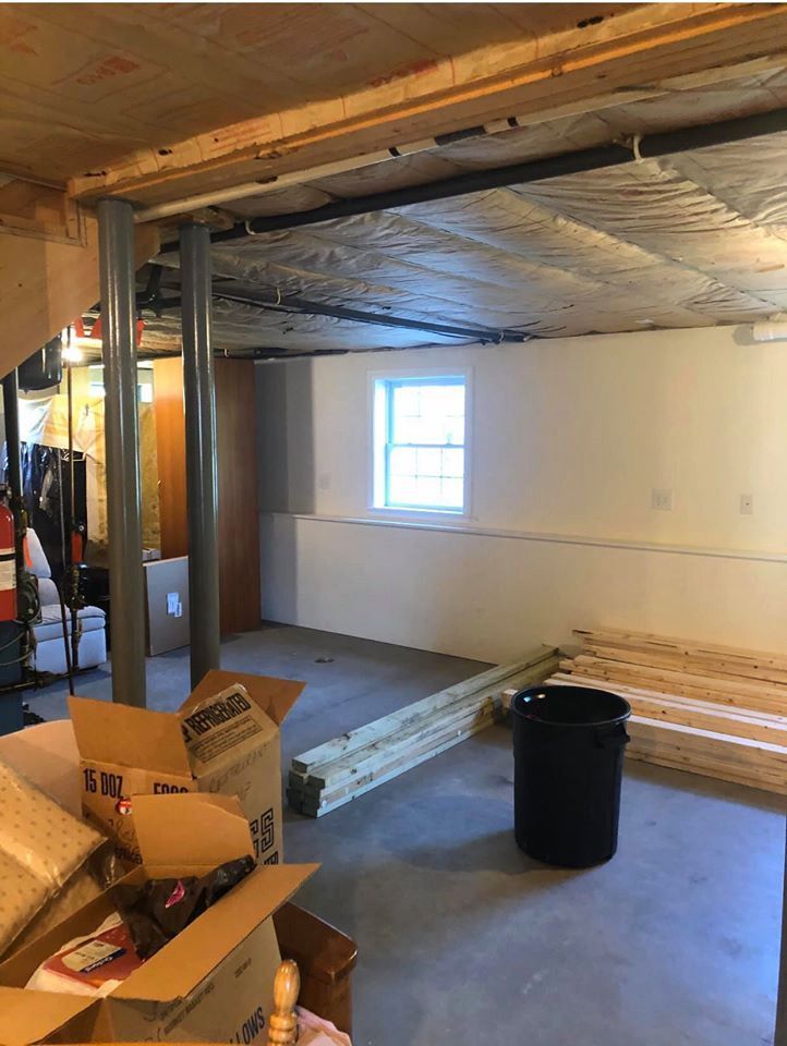 Basement with support beams, unfinished walls, a window, and construction materials on the floor.