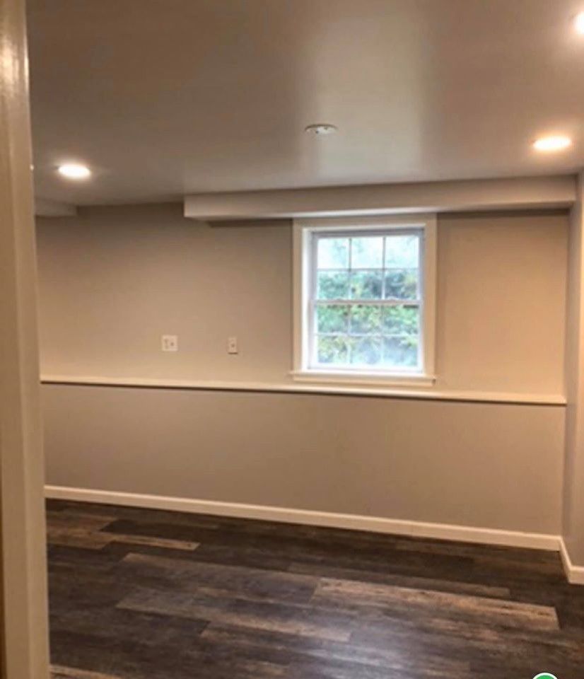 Basement interior with window, neutral walls, dark wood-look floor.