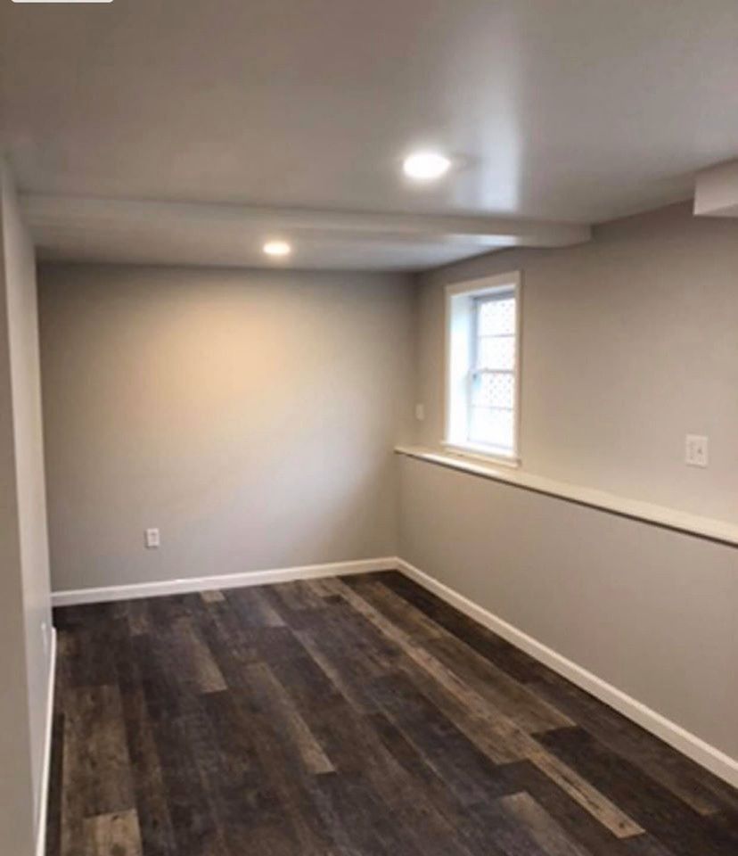 Empty room with wood-look floor, neutral walls, small window, and recessed ceiling lights.