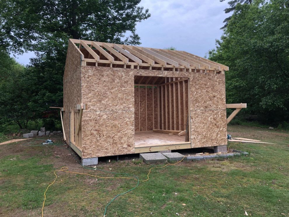 Unfinished shed construction in a grassy yard with a partially built roof and door frame.