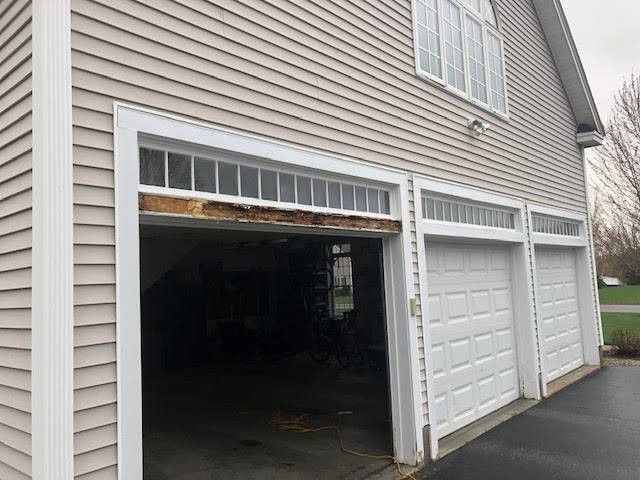Garage exterior with damaged wood above the left door opening; two other garage doors on the right.