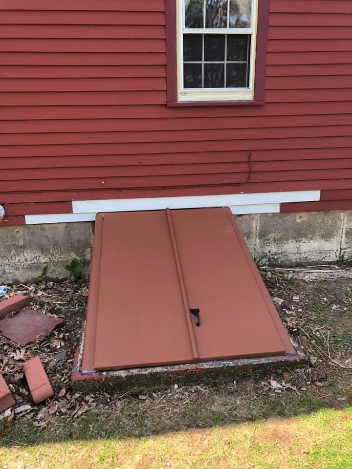 Brown cellar doors against a red house with a white window.