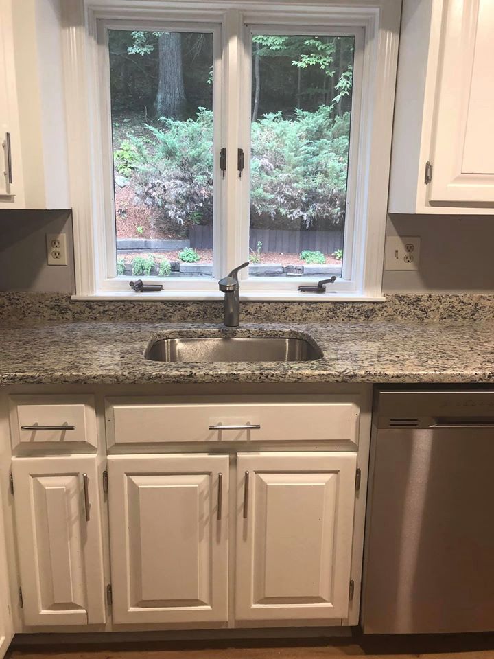Kitchen with a stainless steel sink and faucet, white cabinets, granite countertops, and a window overlooking greenery.