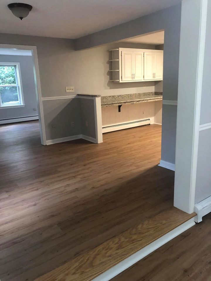An interior view of a remodeled home with wood floors, gray walls, and a kitchen with white cabinets.