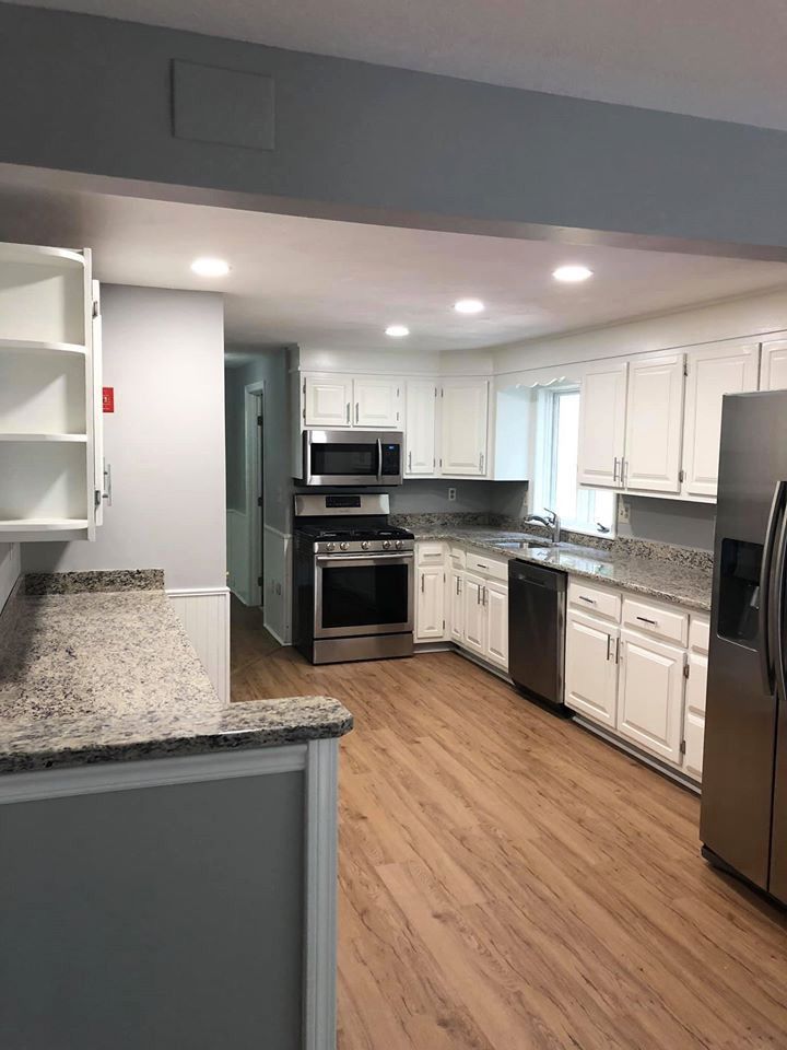 Kitchen with white cabinets, stainless steel appliances, granite countertops, and wood-look flooring.