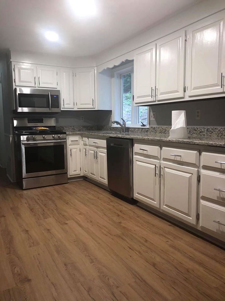 White kitchen with stainless steel appliances, gray countertops, and wood-look flooring.