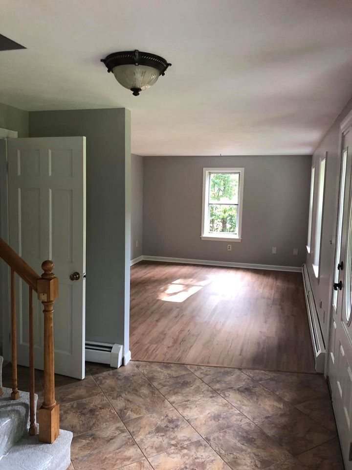 Entryway with staircase and door on the left. A living room with a window and hardwood floors is visible.