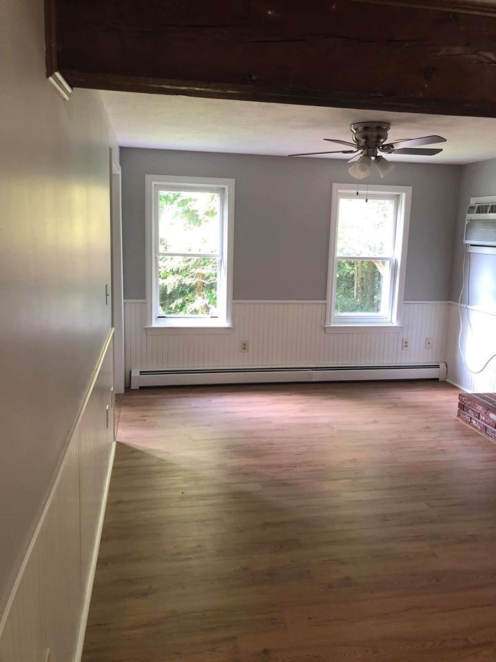Empty living room with wood-look floors, two windows, gray walls, and white wainscoting.