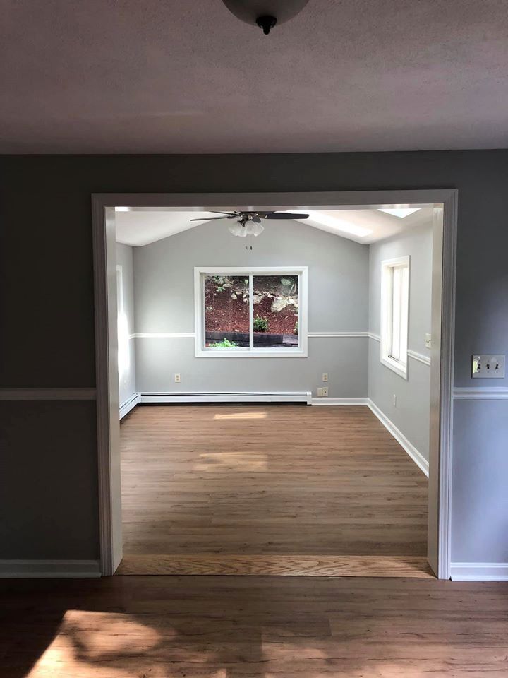 View of an open doorway into a room with wood floors, a window, and gray walls.