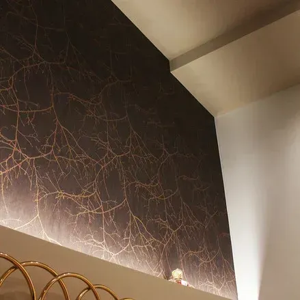 Parete scura con motivo a ramificazioni dorate, con mensola e illuminazione ambientale.