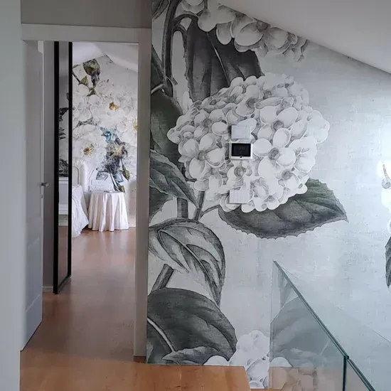 Corridoio con carta da parati floreale, ringhiera in vetro e porta che conduce a un'altra stanza.
