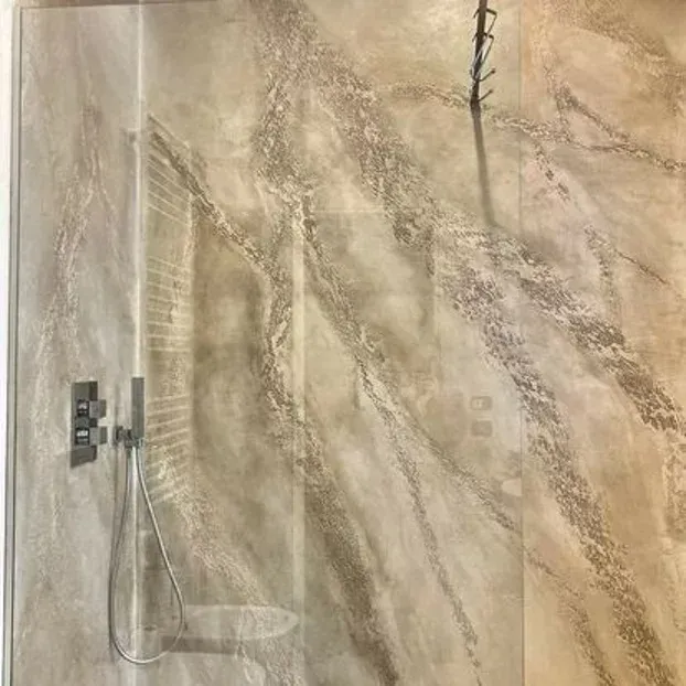 Doccia con pareti effetto marmo e accessori cromati.