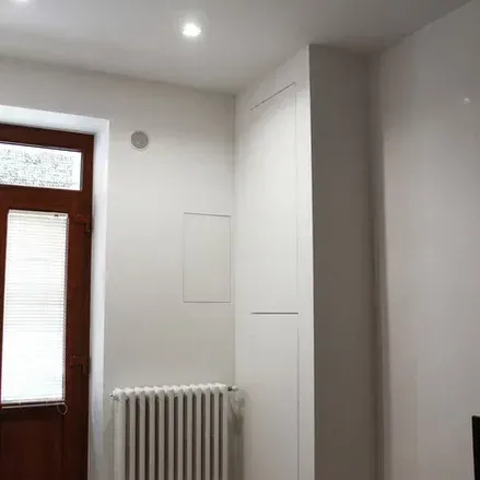 Angolo interno di una stanza con una parete bianca e una porta marrone con persiane. È presente un termosifone.