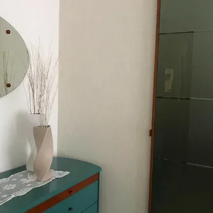 Comò verde acqua con vaso di rametti bianchi. Specchio a parete. Porta dell'armadio verde.