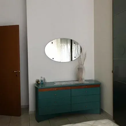 Comò color verde acqua con specchio ovale, vaso e porta marrone su parete bianca.