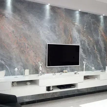 Soggiorno con una grande TV montata su una parete decorativa grigia e color ruggine, mobile bianco sottostante.