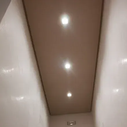Soffitto con tre faretti da incasso. Soffitto beige, pareti bianche e corridoio incassato.