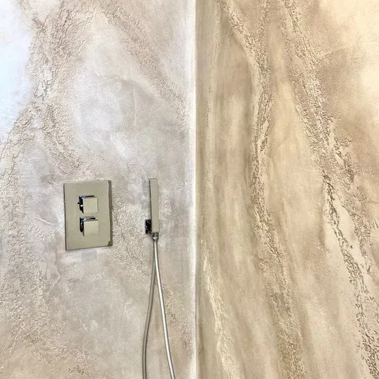 Parete del bagno in beige chiaro con interruttore della luce e soffione della doccia.