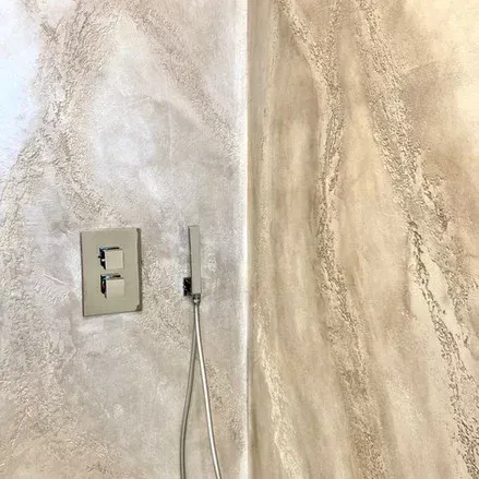 Doccia con pannelli decorativi a parete testurizzati nei colori beige e crema, con comando in acciaio inox e soffione portatile.