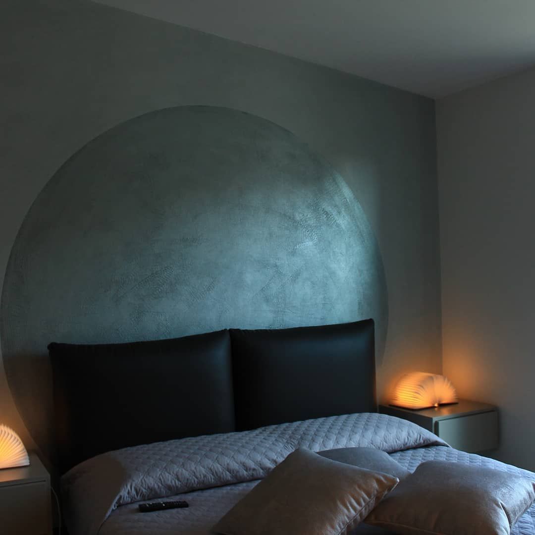 Camera da letto con un grande elemento circolare sulla parete sopra il letto. Due lampade forniscono una luce calda.