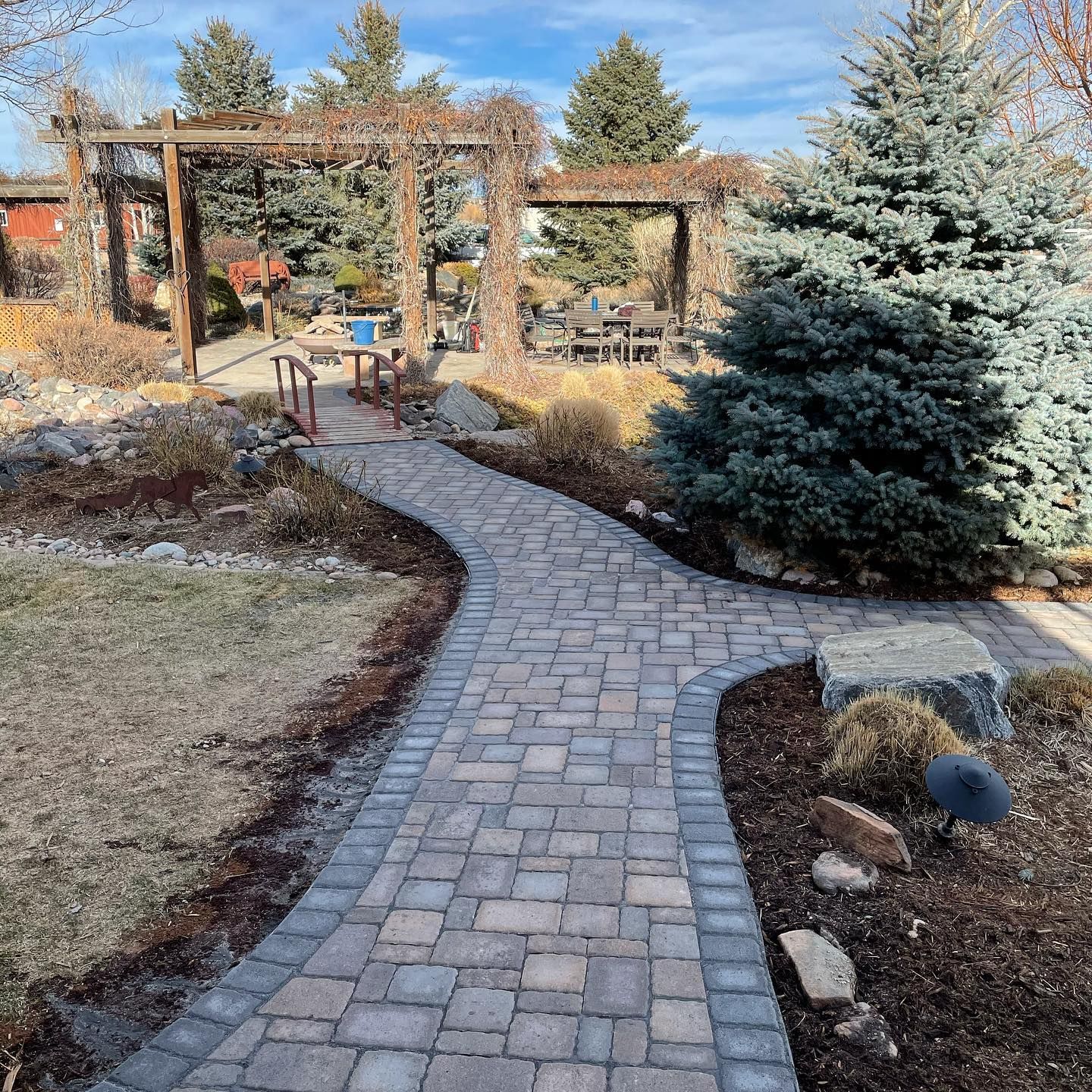 Curved brick garden path leading to a pergola and seating area in a landscaped yard
