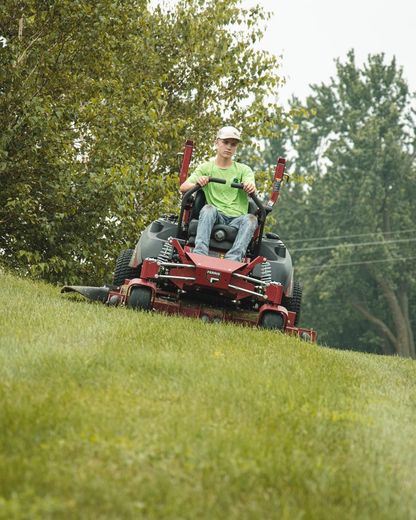Man in a green shirt on a red zero-turn mower mowing a grassy hill.