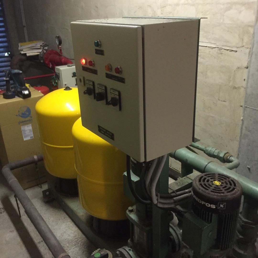 Control panel with switches and lights on a water pump system, yellow tanks, and pipes.