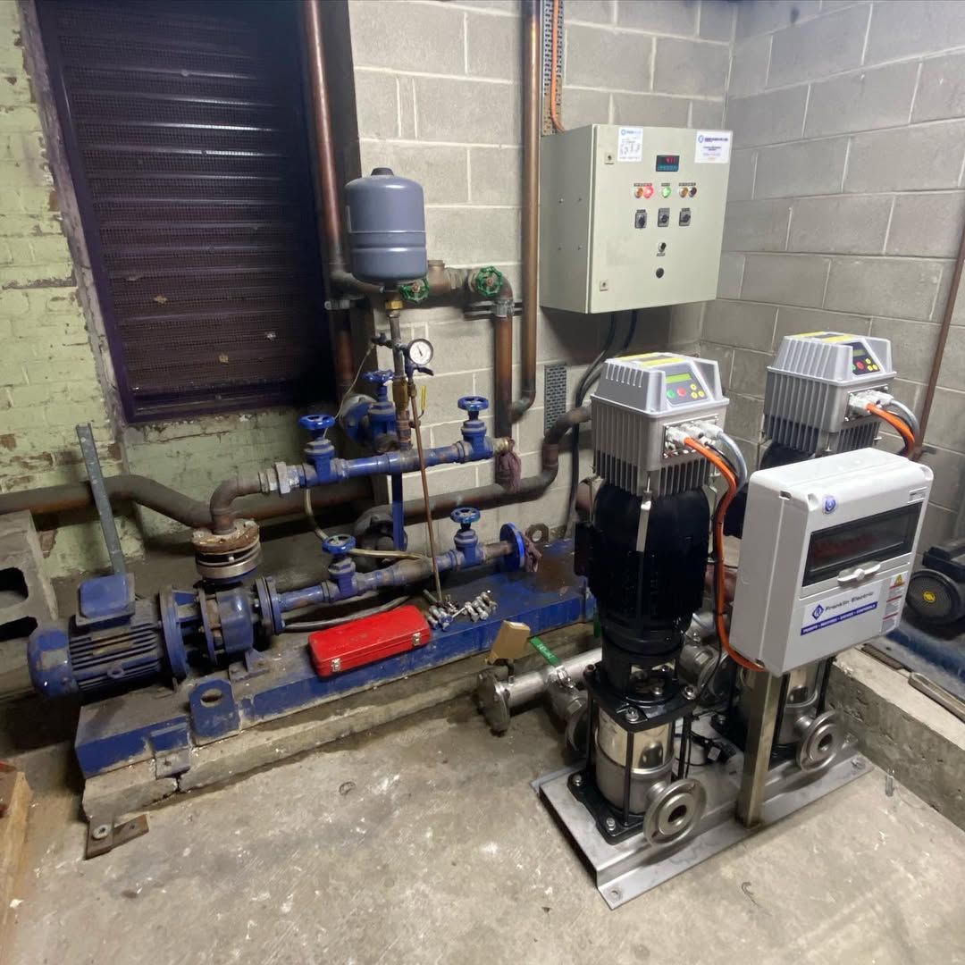 Water pump system with blue and silver components, gauges, and electrical panel in a utility room.