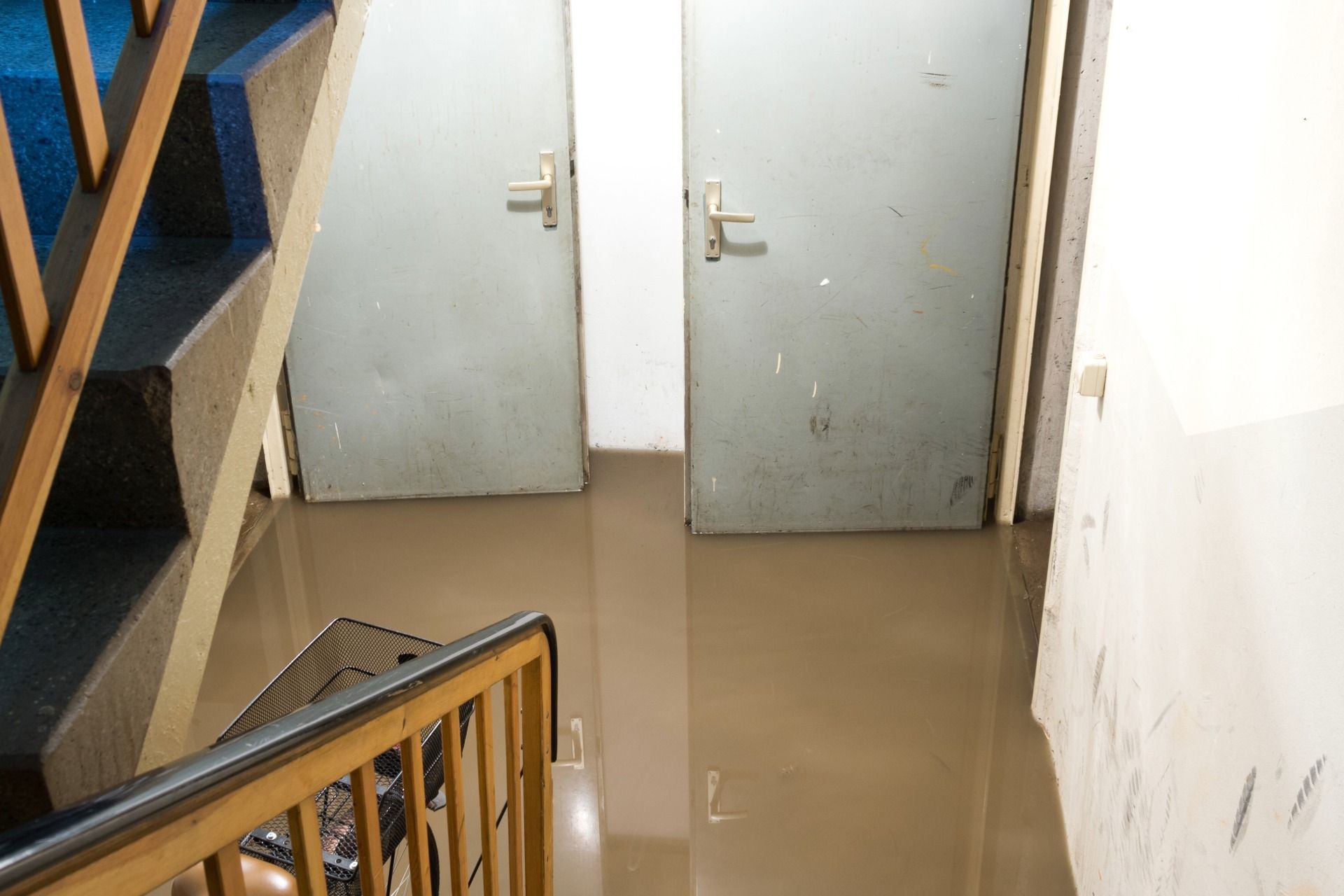 Flooded hallway with two closed doors and a staircase. Brown water covers the floor.