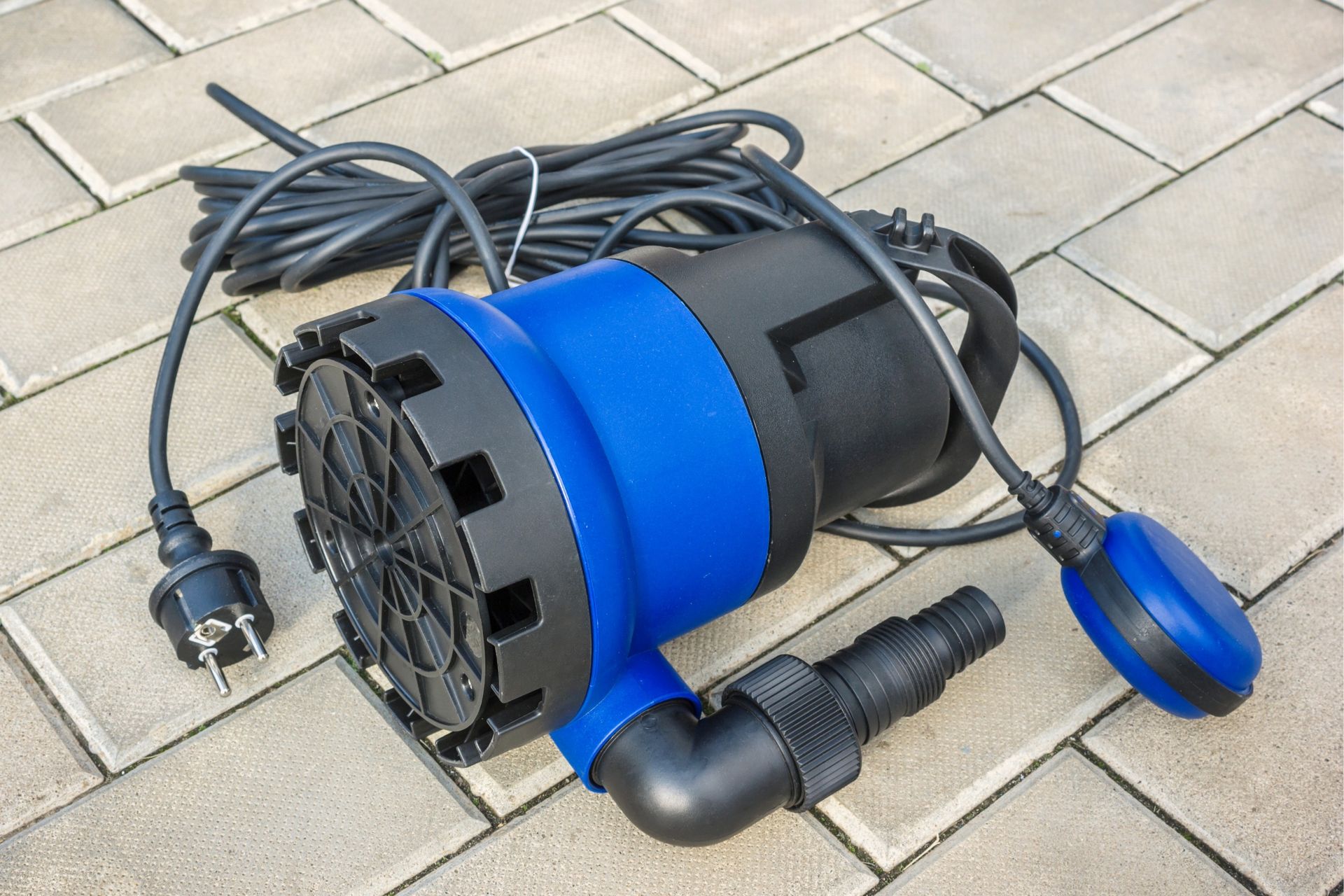 Blue and black submersible pump with attached power cord and float switch on a brick surface.