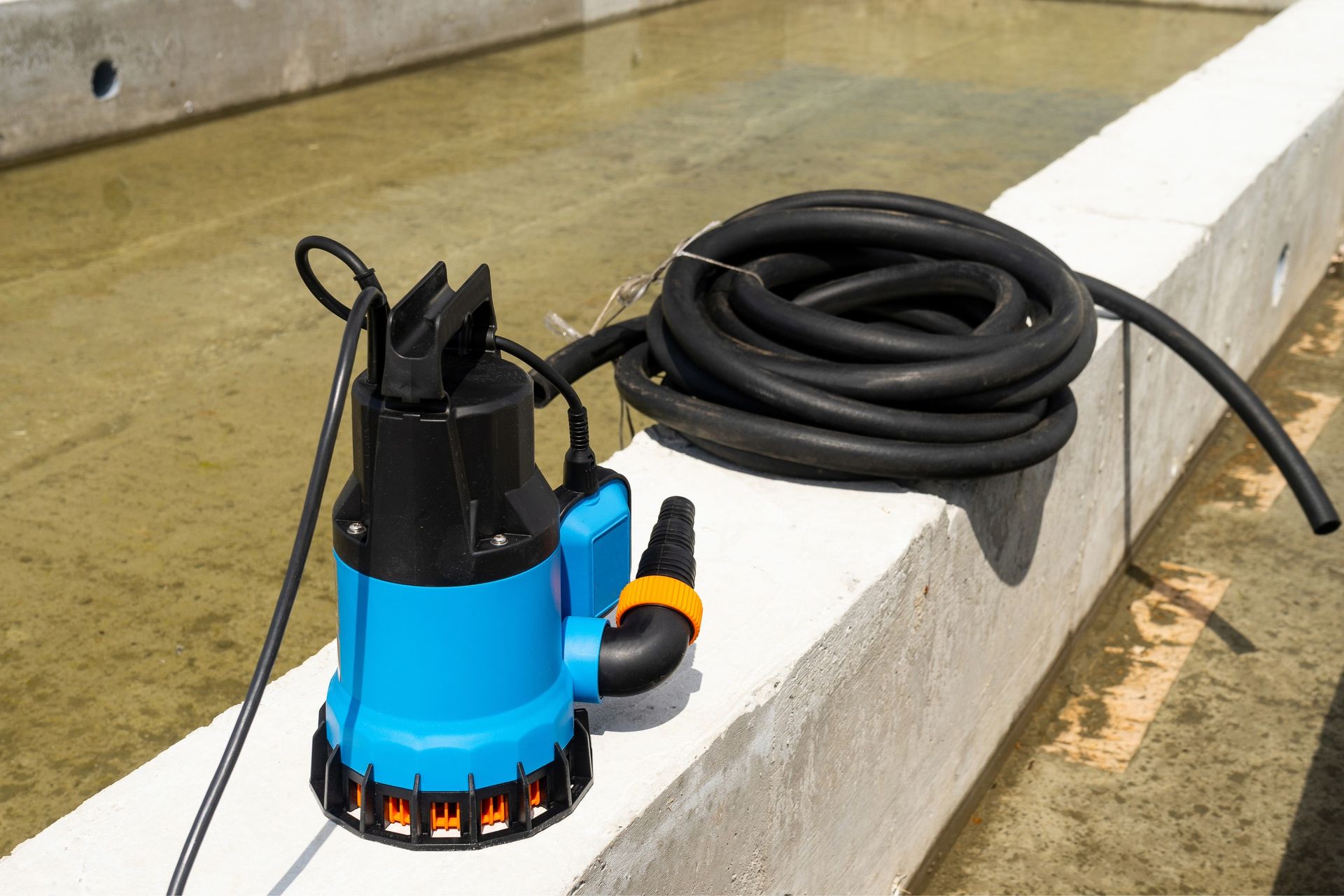 Blue and black submersible water pump with black hose on a concrete edge, near water.
