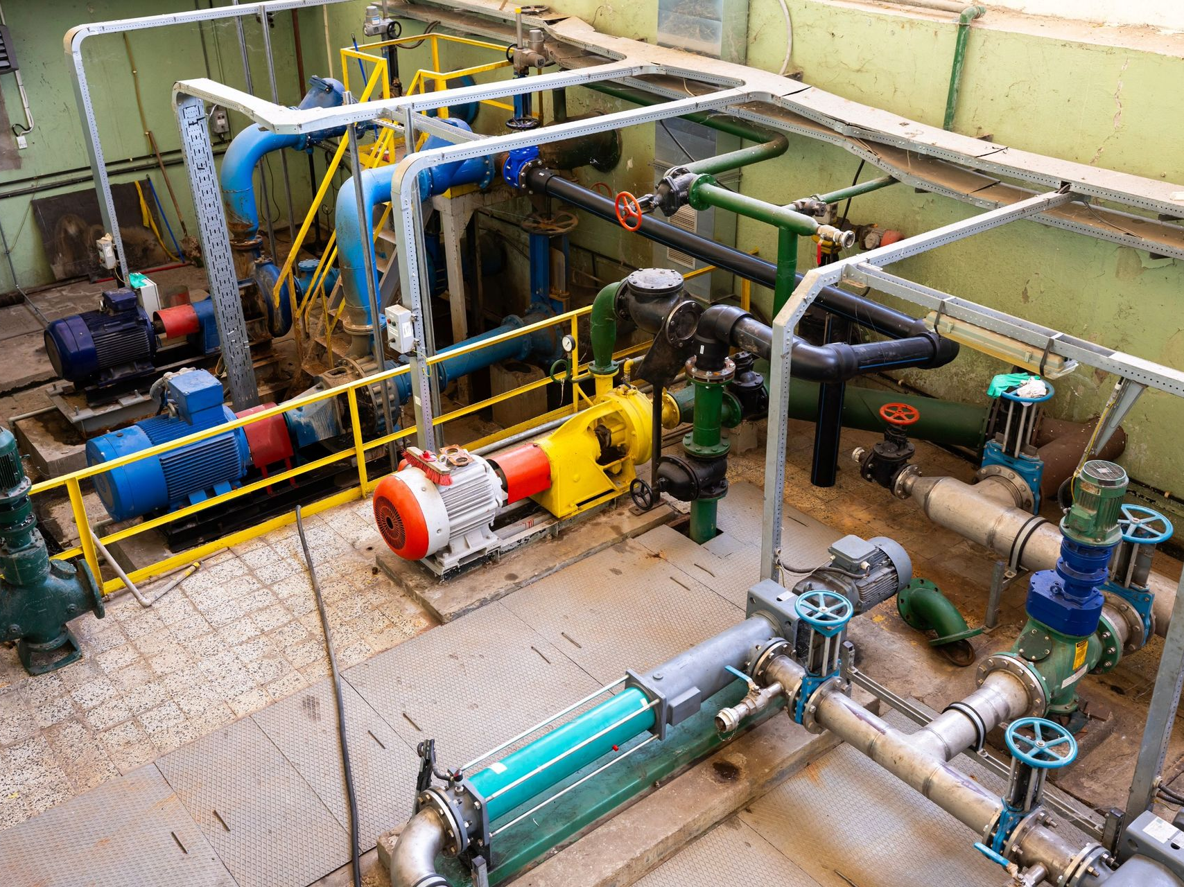 Industrial setting with colorful pipes, pumps, and valves, likely for water or chemical processing.