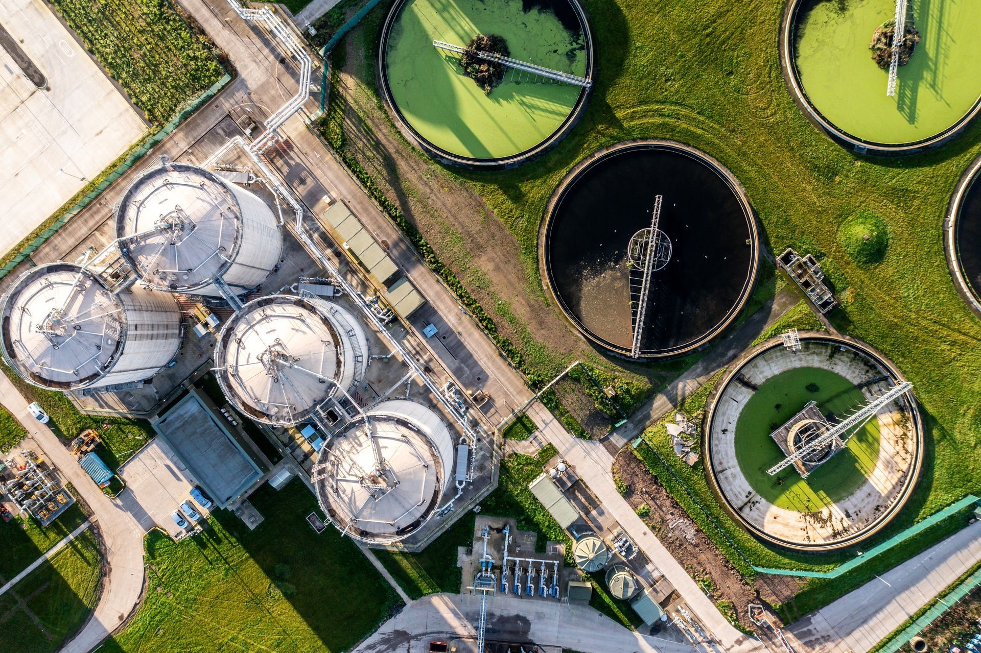 Aerial view of a wastewater treatment plant with cylindrical tanks and circular settling ponds filled with water.