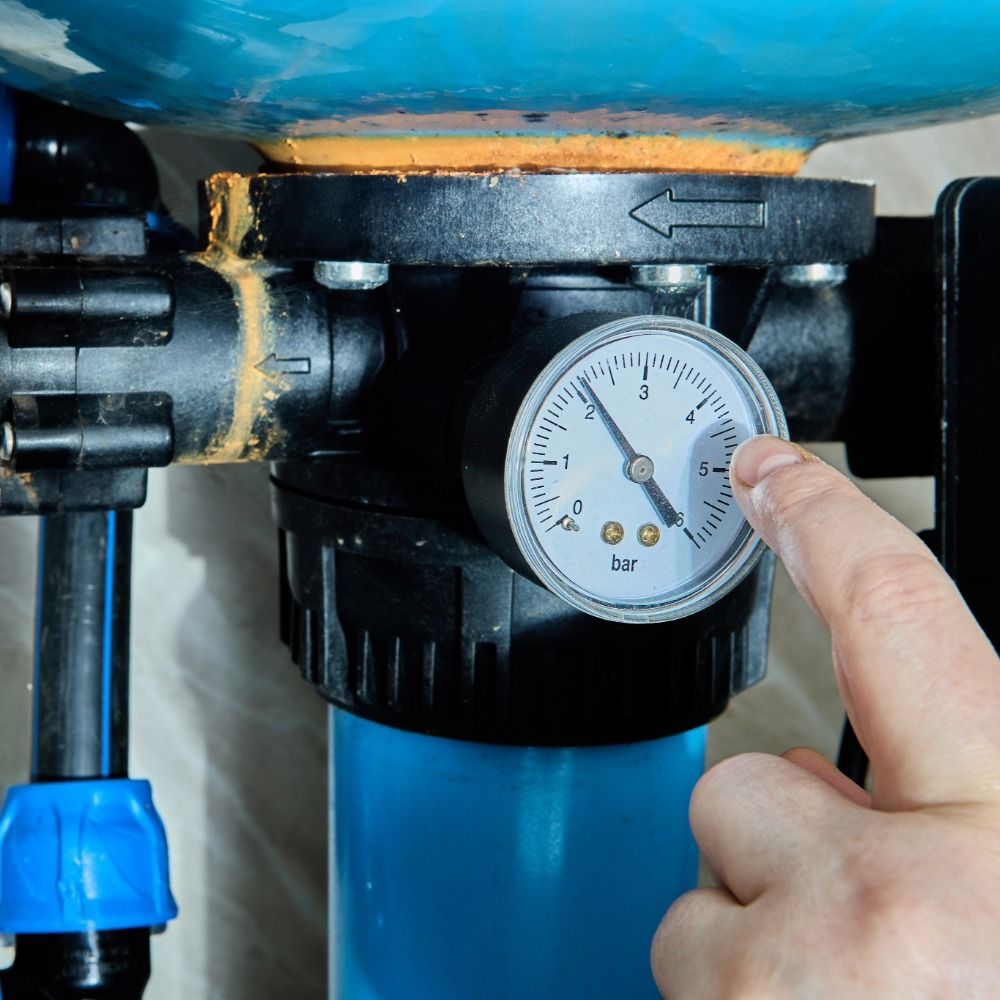 Person's finger pointing at a gauge on a water filter system, showing a pressure reading.