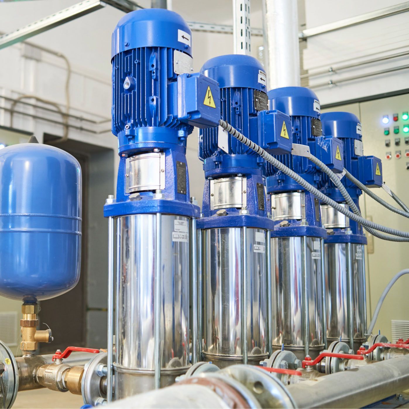 Four blue industrial water pumps, silver cylinders, in a mechanical room setting.