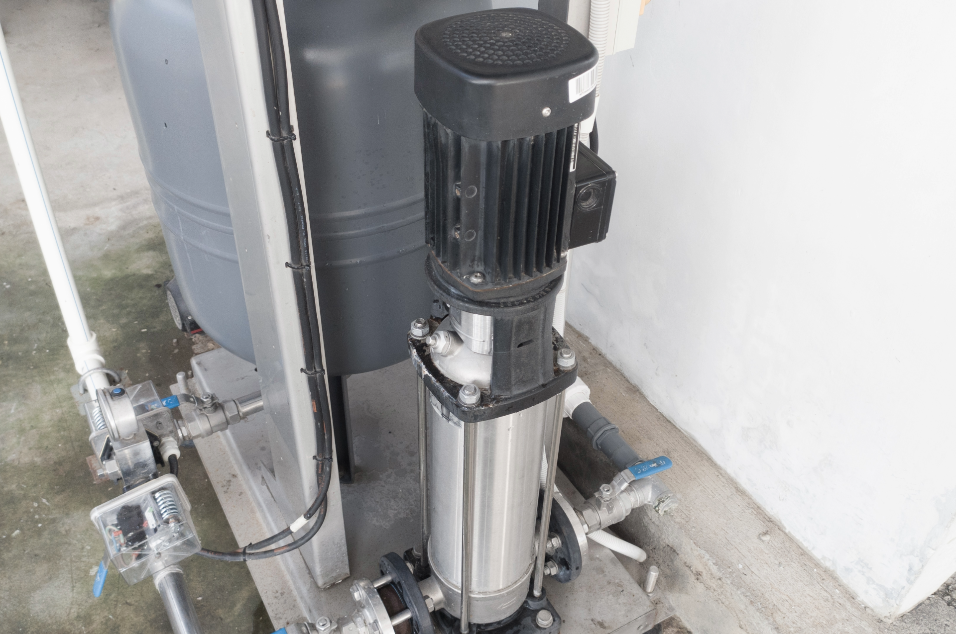 Water pump system with a gray tank and stainless steel pump, outdoors.