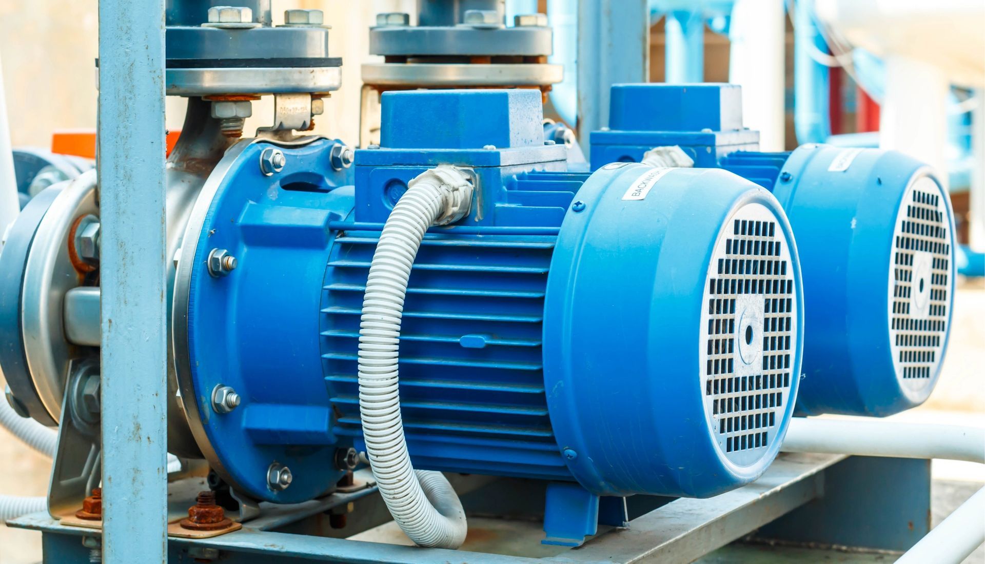 Two blue electric water pumps connected to pipes in an industrial setting.
