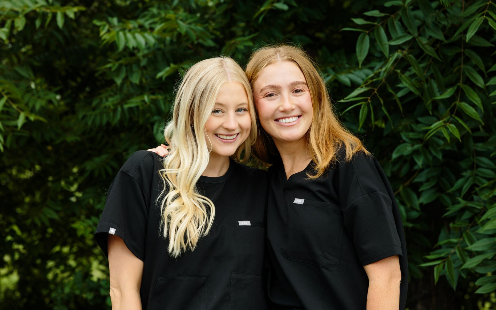 Three smiling women who work at the front desk are posing for a picture together in front of a tree.