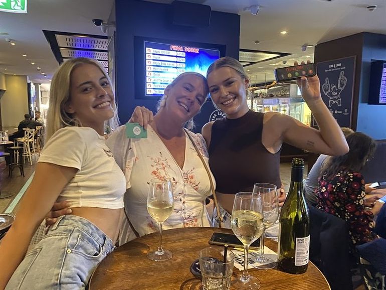 Three women are sitting at a table with wine glasses and a bottle of wine.