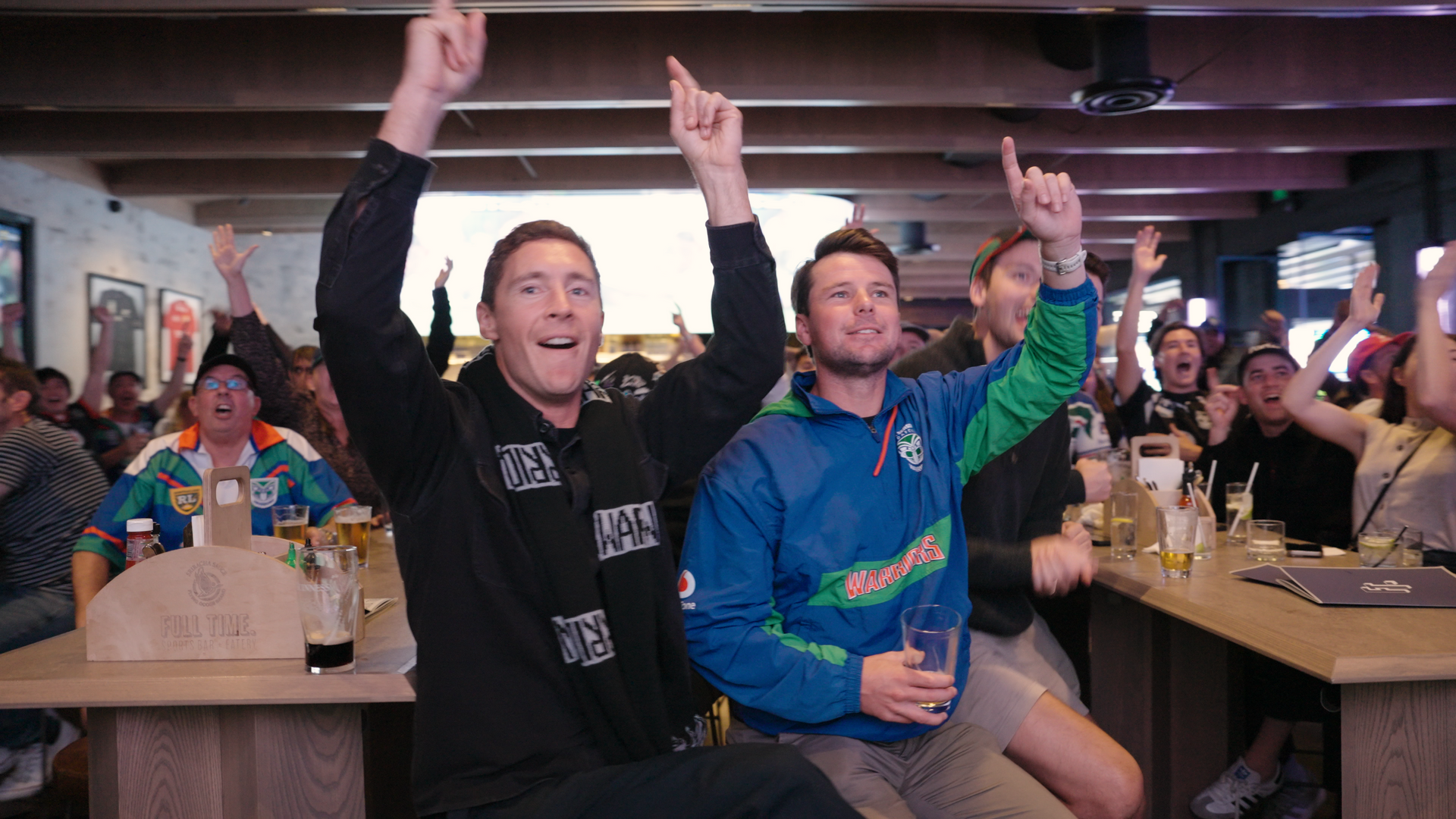 A group of men are sitting at a bar with their arms in the air.