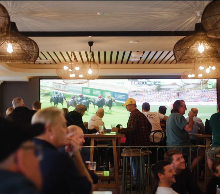 A group of people are watching a horse race on a large screen
