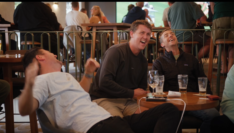 A group of men are sitting at a table in a bar laughing.